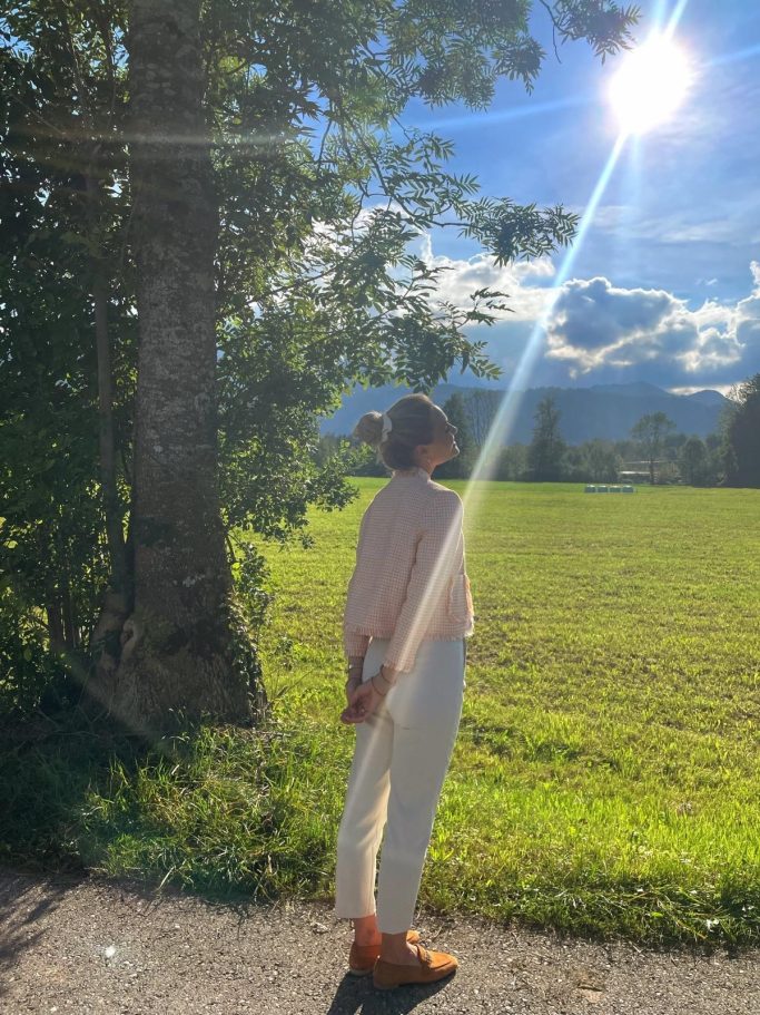 Frau steht im Freien, beobachtet die Sonne über einer grünen Wiese und Bäumen.